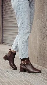 Bota corta de cuero color chocolate, con diseño minimalista, taco cuadrado de 4 cm y una hebilla metálica decorativa en el tobillo sobre una banda de gamuza.