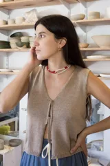 Chaleco de tejido artesanal en color beige, con escote en V y cierre frontal mediante lazos del mismo tejido. Presenta un diseño sin mangas y corte recto con terminación en punto elástico.