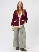 Cardigan de punto grueso con diseño de ochos, color bordó con detalles en beige en la botonera, puños y bolsillos. Presenta un corte oversize, cuello en V y cierre frontal con botones.