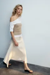 Falda midi de tiro medio color gris, con diseño asimétrico en el bajo, bolsillos frontales y traseros, y cierre frontal con cremallera y botón.