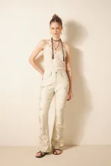 Pantalón de cuero ovino color crema, estilo jeanero con calce flare, adornado con bordados de tachas metálicas y piedras en tonos tierra y dorados a lo largo de las piernas.