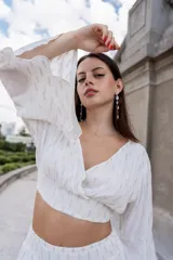 Top corto blanco con lurex plateado, escote cruzado, mangas largas acampanadas y cintura elastizada.