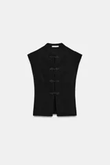 Top de tejido elástico color negro, con cuello mao, manga muy corta y cierre frontal con alamares decorativos.