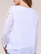 Blusa blanca de gasa liviana con forro interno en el cuerpo, de estilo boho-chic y silueta semi holgada. Presenta escote redondo con canesú de encaje calado en el frente y mangas largas con paneles longitudinales de encaje.