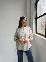 Camisa beige de lino de corte holgado, con cuello mao, mangas largas con puños fruncidos y cierre frontal de botones.