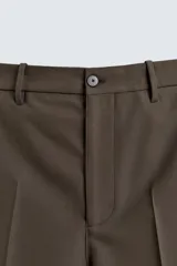 Bermuda de vestir color marrón oscuro, corte relajado y tiro alto, con pliegues frontales y cierre de botón y cremallera.