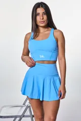 Conjunto deportivo compuesto por un top de escote redondo y una pollera short con diseño acampanado, ambos en color celeste. El top presenta el logo de la marca estampado en el frente.