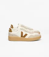Championes Veja modelo V-90, de diseño urbano con combinación de tonos crema, blanco y marrón. Presentan el logo lateral en forma de V, refuerzos de gamuza en la puntera y el talón, y una suela de goma color caramelo.