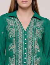 Camisa de estilo boho, color verde, con cuello camisero, escote en V y botonadura frontal con botones perlados. Cuenta con una pechera con bordados geométricos y florales a contraste, mangas largas abullonadas con puños abotonados y delicados bordados dispersos.