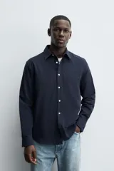 Camisa de corte regular fit confeccionada en tejido de algodón con textura. Presenta cuello solapa, cierre frontal de botones, manga larga con puños abotonados y un bolsillo plastrón en el pecho.