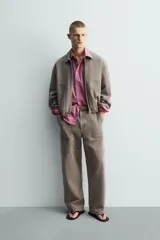 Pantalón de corte relajado en color marrón con efecto lavado. Presenta bolsillos frontales tipo cargo, cierre con cremallera y botón, y una línea horizontal de tachas metálicas a tono en la parte superior de las piernas.