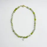 Collar de cuentas de serpentina de 8 mm en tonos verdes, con nudos separadores de hilo verde y un dije central de perla de río natural. Cuenta con broche y terminaciones en acero con baño de oro.