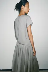 Vestido midi de Zara Woman Collection confeccionado en hilatura con lino, color gris. Presenta cuello redondo, manga corta caída, detalle de frunces y lazadas laterales en el mismo tejido, y cierre en la espalda.