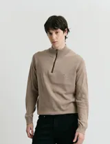 Sweater de punto color verde oliva, con cuello alto y medio cierre frontal. Presenta coderas en símil nappa y puños acanalados.