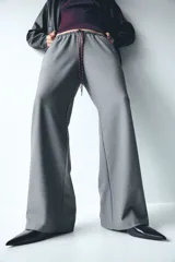 Pantalón de corte holgado color gris, con cintura elástica y cordón de ajuste trenzado en tonos rojo y blanco. Presenta piernas rectas y bolsillos laterales.