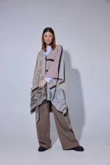 Ruana tejida en lana lambswool con diseño de bloques de color y tramas geométricas. Presenta cierre frontal con doble cursor y tiradores de cuero, permitiendo diferentes formas de uso.