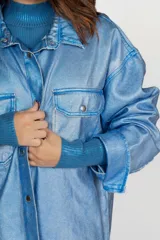 Sobrecamisa de jean color celeste con efecto metalizado, de corte holgado, con cuello camisero, botones frontales y dos bolsillos con solapa en el pecho.