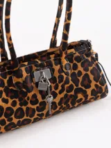 Cartera de hombro de cuero vacuno con pelo y estampado animal print de leopardo. Cuenta con herraje metálico tipo lock con llave colgante, asas largas y tiras laterales ajustables.