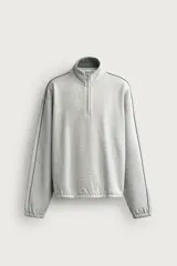 Sudadera gris de corte relaxed fit confeccionada en tejido con algodón, con cuello subido y cierre frontal de cremallera parcial. Presenta manga larga con costura combinada a contraste y acabados en elástico en puños y cintura.