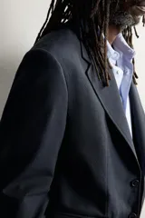 Blazer regular fit de lana color negro, con cuello de solapas de muesca, manga larga con botones en los puños y cierre frontal de botonadura. Cuenta con bolsillos de vivo en el pecho y de solapa en la cadera. Colección especial Aaron Levine x Zara.
