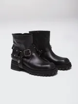 Bota corta de cuero negro con punta cuadrada, suela track y detalle de estribo desmontable con hebilla metálica.