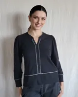 Remera de algodón color negro, con mangas largas ligeramente abullonadas en los hombros y puños ajustados. Presenta un escote en V con detalle de costuras decorativas en color contrastante que recorren el frente y el ruedo.