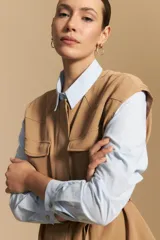 Camisa de corte clásico y holgado, confeccionada en tela blanca, con cuello camisero, cierre frontal de botones de nácar y mangas largas con puños abotonados.