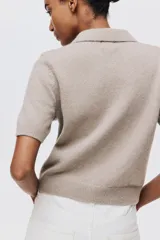 Saco de manga corta en punto suave color beige, con cuello camisero, cierre frontal de botones con strass y terminaciones acanaladas en mangas y bajo.