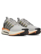 Championes Under Armour Phantom X, de color gris con detalles en naranja y suela blanca y negra. Presentan una estructura de soporte lateral semitransparente con el logo de la marca y cordones con detalles amarillos.