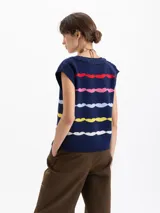 Chaleco de punto azul marino con escote en V y bordes trenzados. Presenta un patrón de ondas horizontales en colores rojo, rosa, azul claro, amarillo y blanco. Incluye un bordado tipo escudo en el frente.