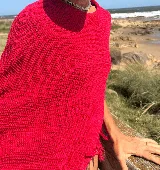 Poncho rojo tejido en hilo de algodón con lurex y flecos en el borde inferior.