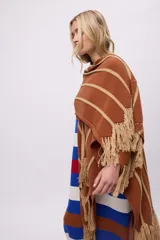 Ruana tejida de punto color terracota con franjas horizontales y diagonales en color beige. Presenta flecos largos en los bordes.