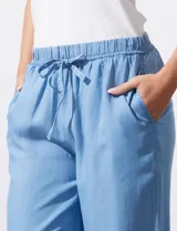 Pantalón celeste de lyocell, corte ancho, con pretina elastizada con lazo de ajuste, bolsillos verticales y ruedo desflecado.
