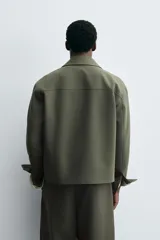 Sobrecamisa de corte boxy fit confeccionada en tejido compacto color beige, con cuello solapa, cierre frontal de botones y bolsillos laterales en costura.