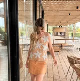 Chaleco de cuero tostado en el frente con apliques de grandes flores de crochet blancas, y espalda de tejido de punto de algodón. Presenta cuello redondo y diseño sin mangas.