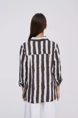 Camisa de manga larga con cuello clásico y cierre frontal de botones. Presenta un estampado de rayas verticales irregulares en tonos oscuros, blancos y verde claro.
