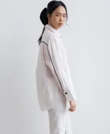 Camisa negra de manga larga, con cuello camisero y botones frontales. Presenta aberturas laterales en el ruedo.