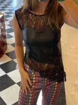 Top sin mangas confeccionado en una combinación de cuero genuino y encaje negro. Presenta un diseño de escote redondo con detalle de encaje en la parte superior y en el ruedo, con una terminación asimétrica e irregular.