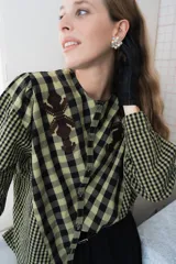 Blusa de algodón con estampado a cuadros en tonos azul y negro, con bordados decorativos en color bordó sobre el canesú. Presenta cierre frontal con botones, cuello redondo y mangas largas levemente abullonadas.