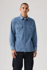 Camisa de pana color azul claro, con cuello clásico, cierre frontal de botones y dos bolsillos con solapa en el pecho.