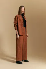 Pantalón de corte ancho y silueta relajada, confeccionado en tejido de efecto gamuzado color marrón oscuro. Presenta un diseño de tiro alto con cierre frontal y bolsillos laterales.