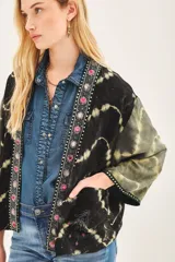 Kimono de estilo abierto con mangas amplias, confeccionado en viscosa con técnica de teñido tie-dye en tonos negro y verde oliva. Presenta una guarda frontal bordada con detalles de pedrería y apliques decorativos.
