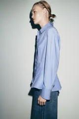Camisa de algodón con cuello solapa, manga larga con puños y diseño peplum en el bajo. Presenta cierre frontal con botones ocultos por solapa.