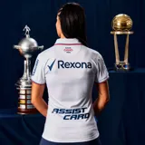 Camiseta de fútbol Umbro del Club Nacional de Football, modelo Home 2026, para mujer. Diseño en color blanco con sutil estampado jacquard, cuello polo con detalles en azul y rojo, y logo de la marca junto al escudo del club en el pecho.