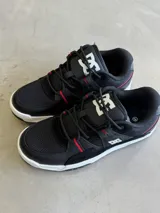 Championes DC modelo Manteca 4, color negro con detalles en rojo y blanco. Presentan una combinación de materiales que incluyen malla transpirable y cuero sintético, con el logo de DC en la lengüeta y una suela blanca.