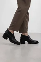 Botín asimétrico de estilo Chelsea color bordó, confeccionado en cuero vacuno, con paneles elásticos laterales negros, puntera cuadrada, suela de plataforma y tacón de bloque cuadrado.