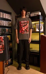Remera de manga corta con cuello redondo y calce oversize, color gris oscuro. Presenta un estampado frontal con estética retro que incluye figuras humanas y una computadora antigua en tonos rojos.