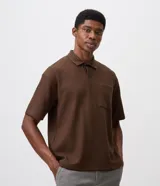 Remera polo de manga corta y corte regular, confeccionada en tejido texturizado color marrón, con cuello camisero, cartera corta con botones y un bolsillo aplicado en el pecho.