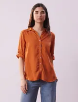 Camisa color beige de tencel, marca Hester & Orchand, con cuello con solapa, escote en V, abertura central con botones y bolsillos delanteros. Las mangas son largas y regulables con presilla y botón.