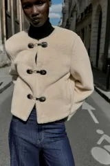 Chaqueta de cuello redondo y manga larga con tejido exterior efecto pelo e interior efecto ante. Presenta bolsillos delanteros de vivo y cierre frontal con alamares metálicos.